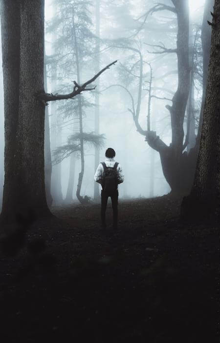 a man standing in a dark forest with a backpack