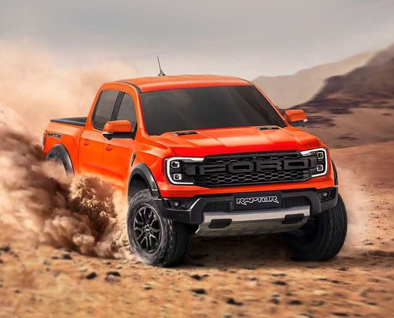 Orange Ford F-150 Raptor performance truck driving through desert sand dunes off-road.