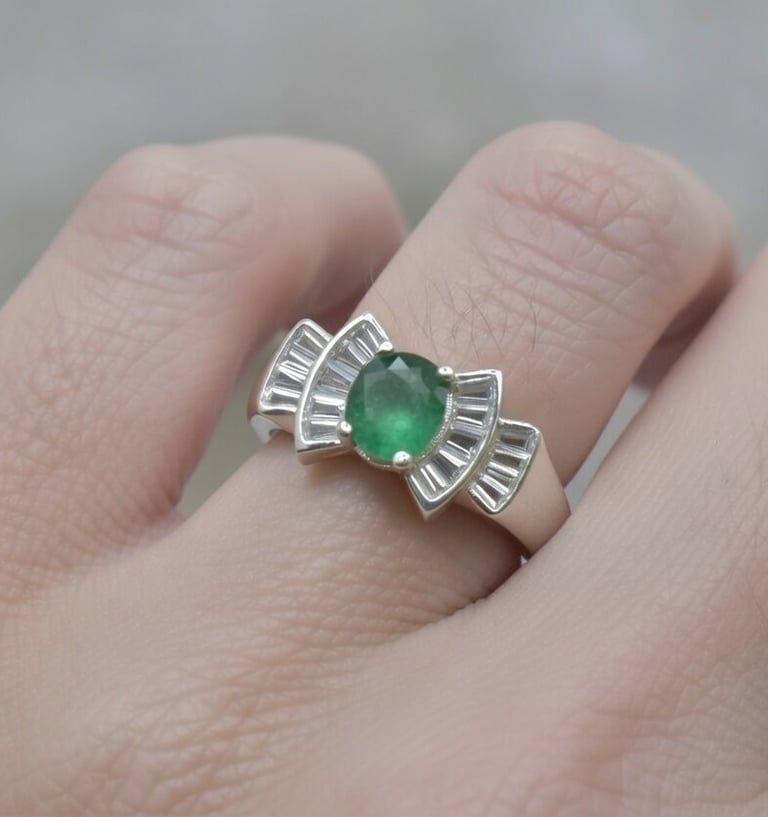 Hand wearing a vintage silver ring with an oval emerald gemstone and tapered baguette diamond accents.