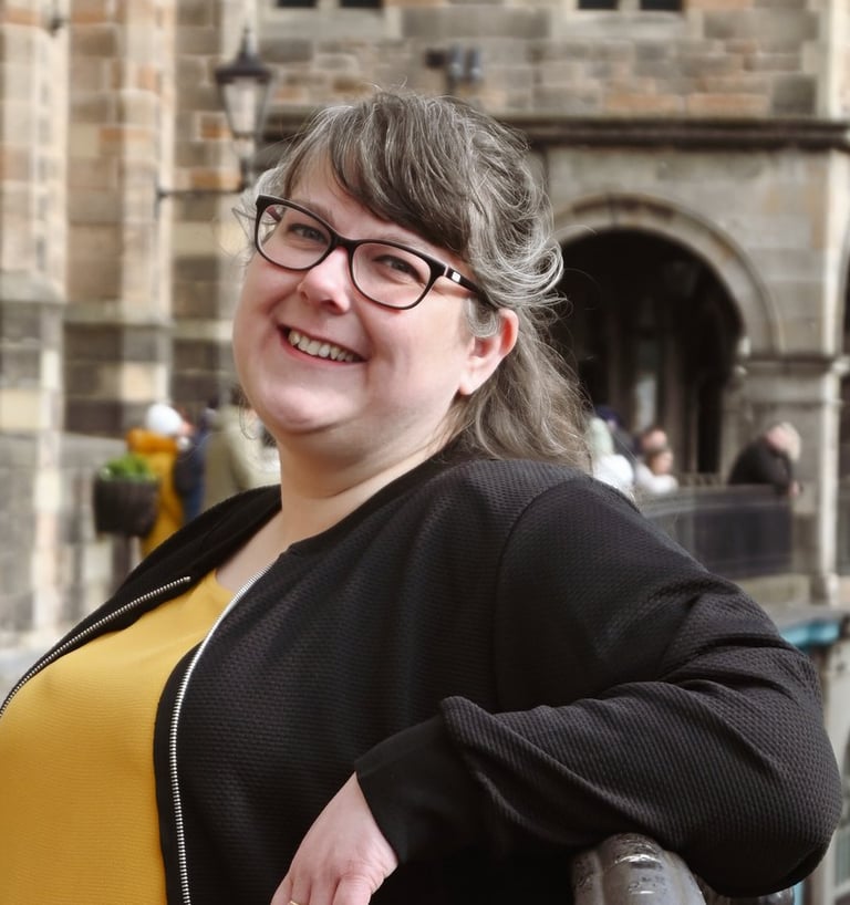 Laura is leaning against a railing and smiling at the camera