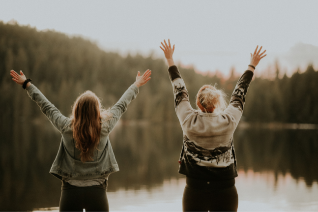 Two happy people with arms raised, standing by a lake, celebrating the positive impact of care from Archway Mental Health.