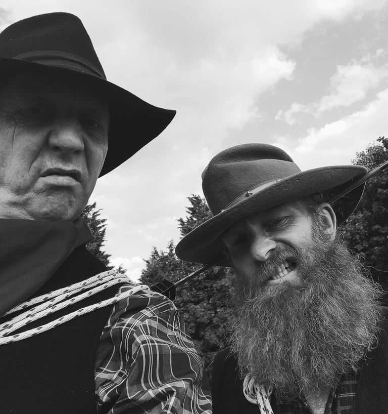 Two men wearing vintage cowboy hats and western attire in a black and white portrait.