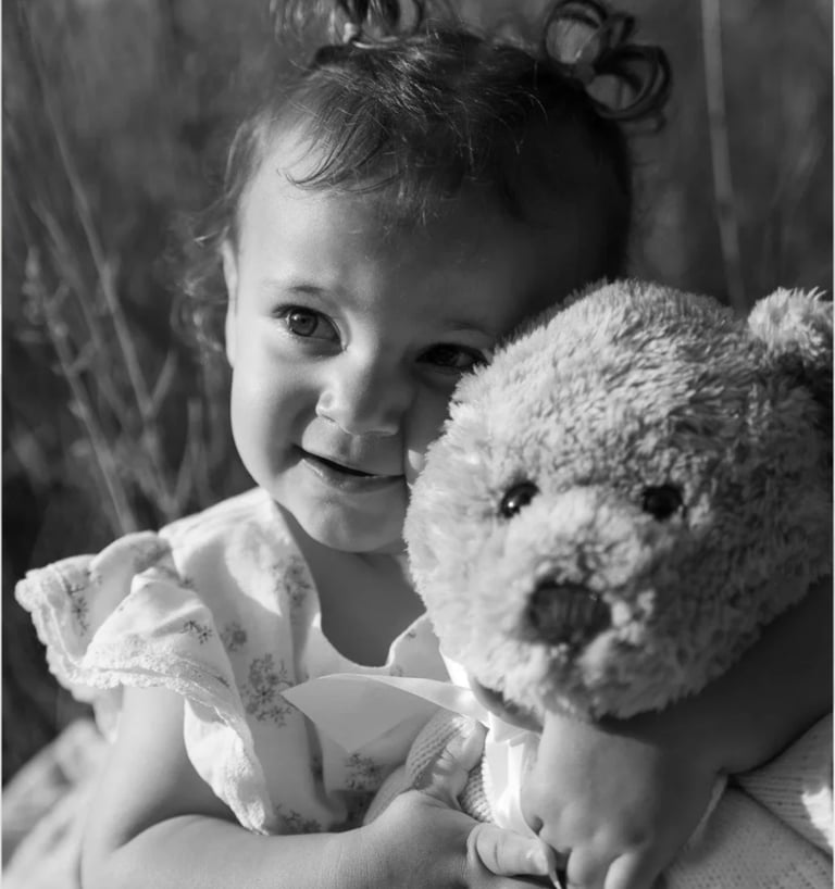 Black and white portrait of a smiling toddler holding a teddy bear during a family photoshoot.