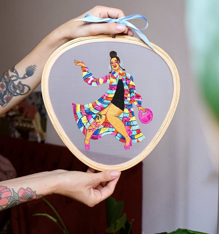a person holding a embroidery hoop with a fashion illustration embroidered