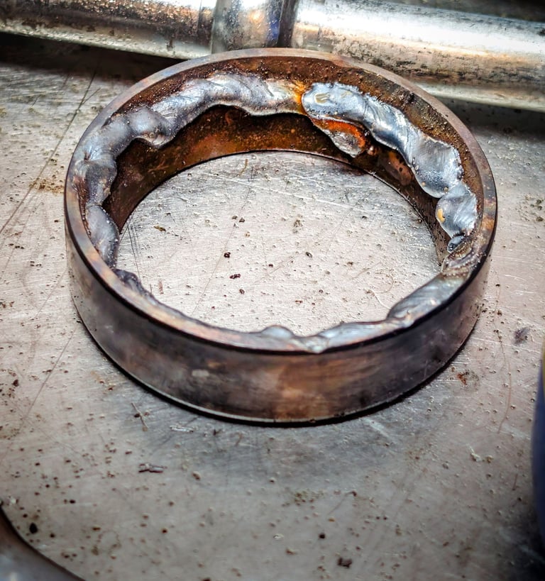 A metal bearing race with weld beads on the inner diameter for removal on a steel workbench.