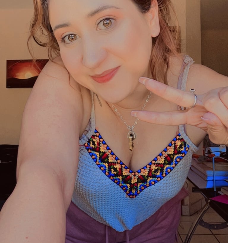 Una mujer sonriente con un top bohemio azul con bordados coloridos haciendo el signo de la paz.