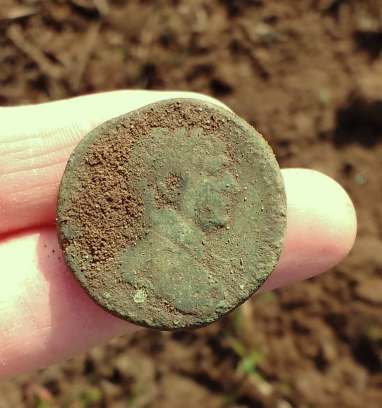 A large Roman coin with green patina, held out on two fingers of the finder.