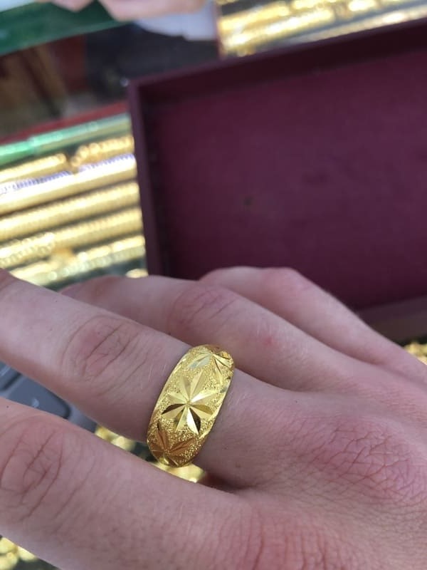 Ein goldener Ehering mit sternförmigem Muster, der in einem Juweliergeschäft an einer Hand getragen.