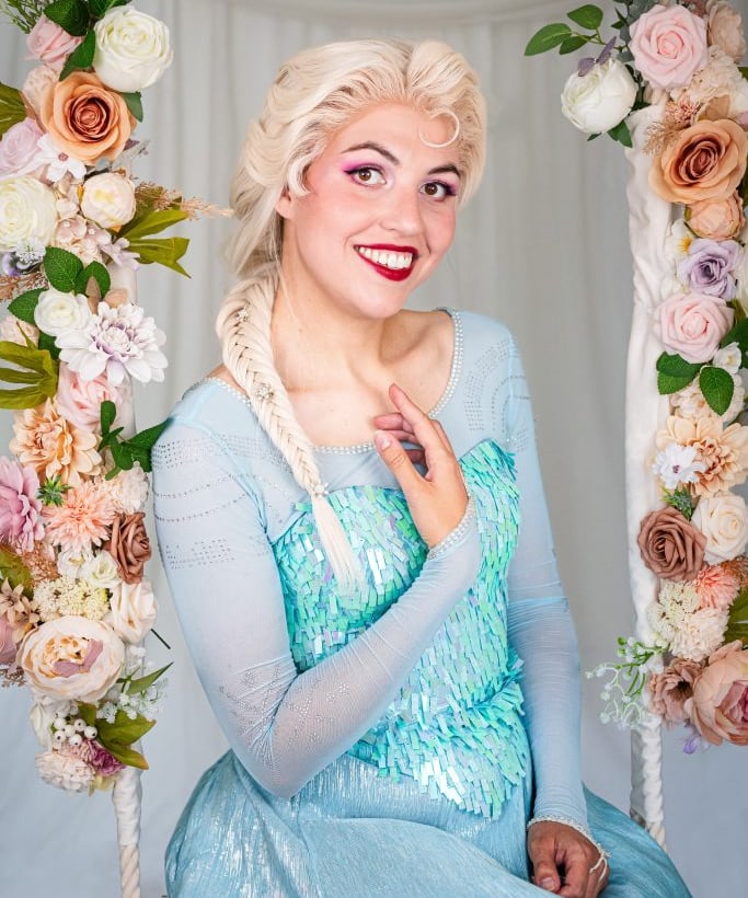 Een lachende ijskoningin in een lichtblauwe glitterjurk zit op een schommel versierd met bloemen.