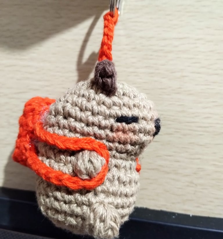 Llavero amigurumi de capibara marrón hecho a mano en ganchillo, con mochila naranja.