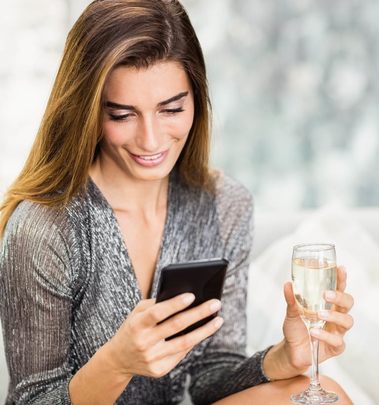 Jolie jeune femme tenant dans sa main gauche une flûte de Champagne et dans l'autre un téléphone