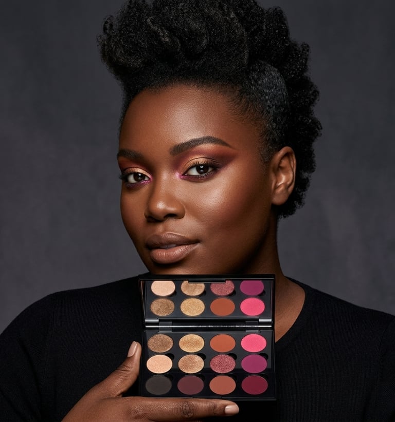 A model with a mohawk hairstyle holding a luxury eyeshadow palette with pink and gold shades.
