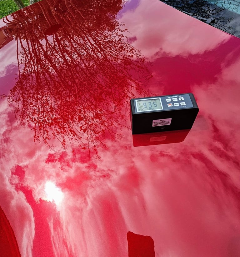 a ceramic coated red car with a gloss meter measuring the gloss factor on the hood of a red car