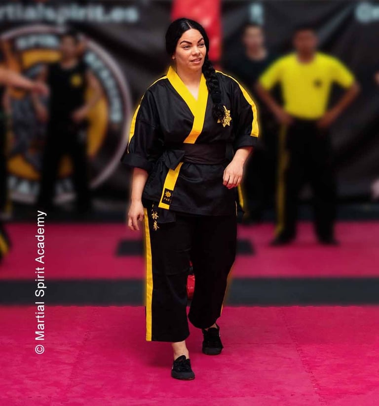 a woman in a black and yellow uniform is standing in a karate pose