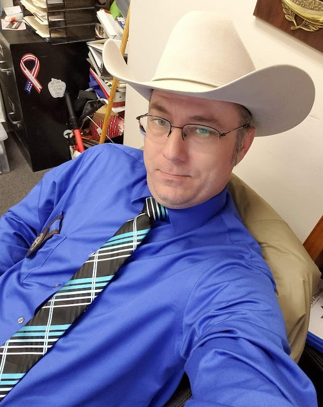 The Author, Steven L Riddles Jr, blue shirt, blue and black tie, with a grey cowboy hat.