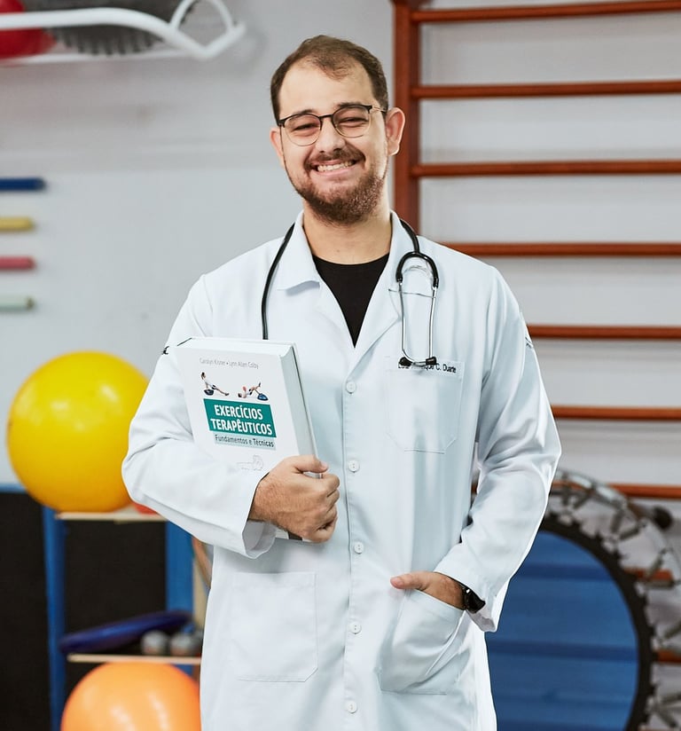 Fisioterapeuta Doutor Luiz Duarte de jaleco branco segurando um livro enquanto sorri