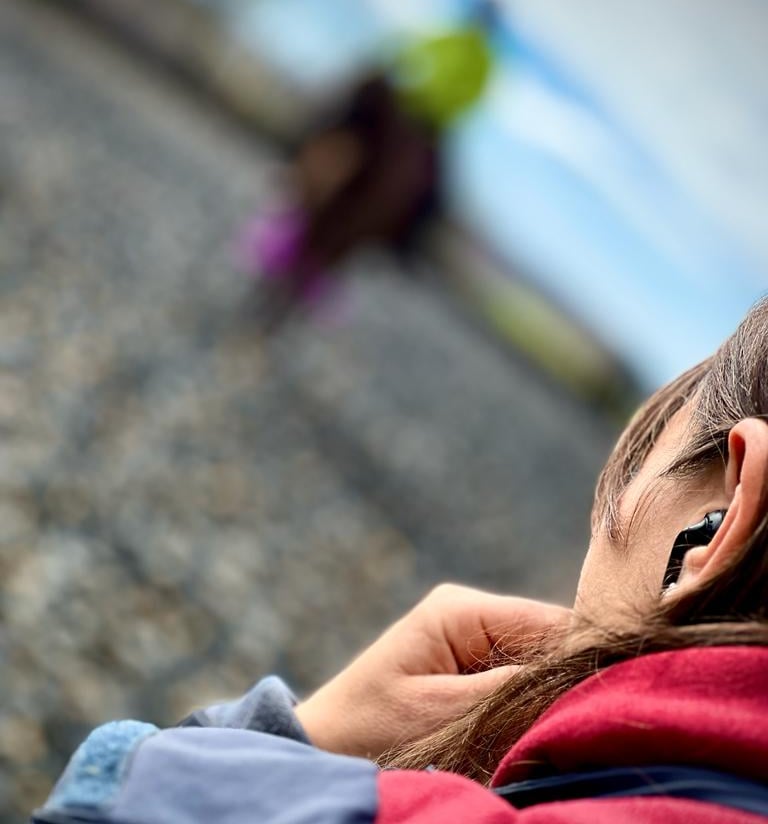 A woman wearing black wireless earbuds while jogging outdoors on a gravel trail.