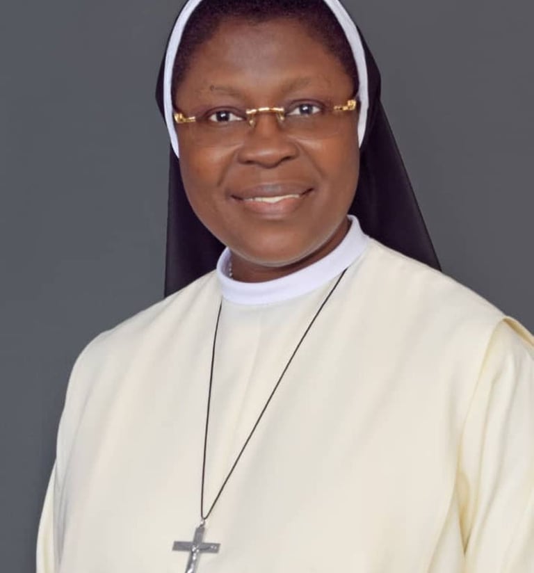 Portrait of a smiling Catholic nun wearing a cream habit, black veil, and silver crucifix necklace.