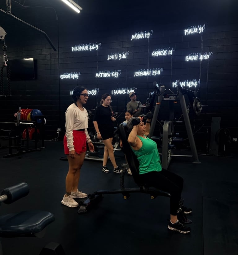 A woman performs a seated dumbbell press at a gym featuring neon Bible verse signs on the wall.