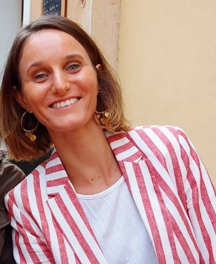 Smiling woman with short brown hair wearing a red and white striped linen blazer and gold hoop earrings.