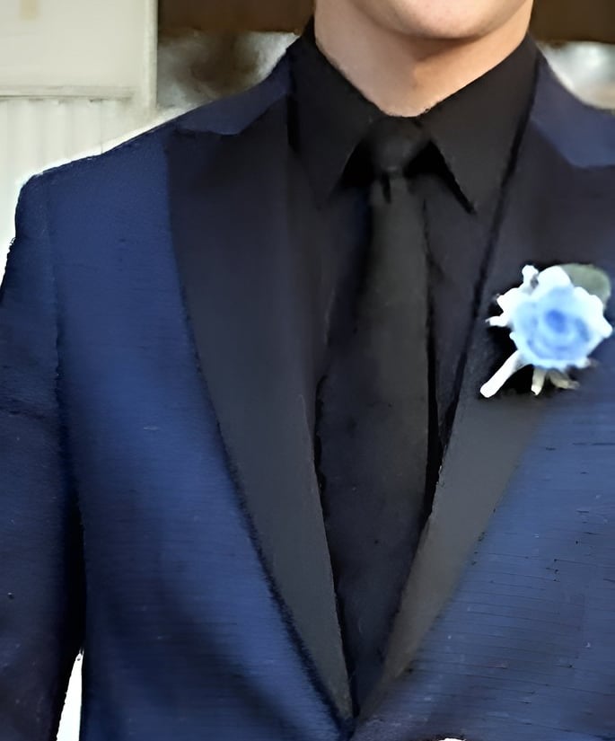 Codie Mills in a navy blue tuxedo with a black lapel, black shirt, and a blue rose boutonniere.