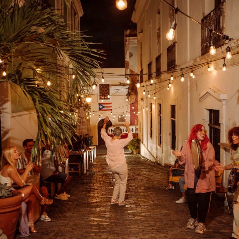 People dancing and playing music in a narrow Old San Juan street decorated with string lights at night.
