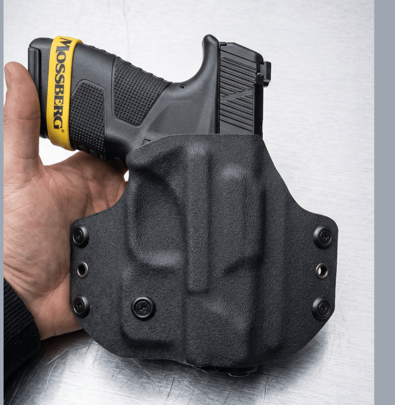 Hand holding a black Mossberg MC2c pistol secured in a custom black Kydex OWB holster.