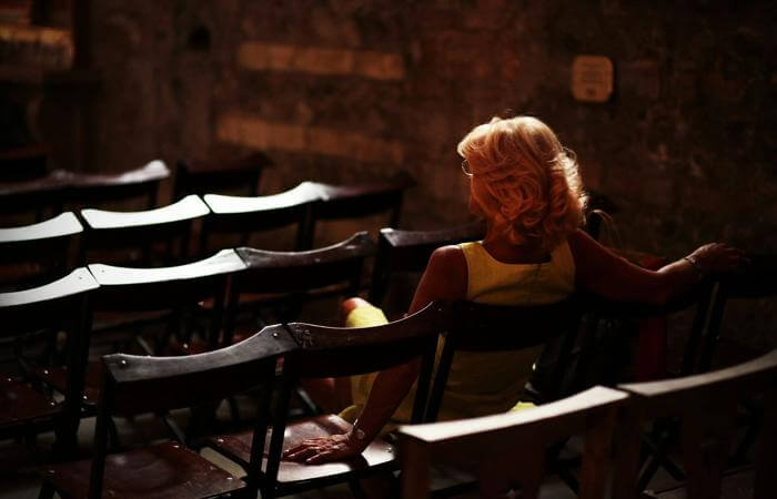 Person in yellow dress seated alone among empty chairs in a softly lit room.