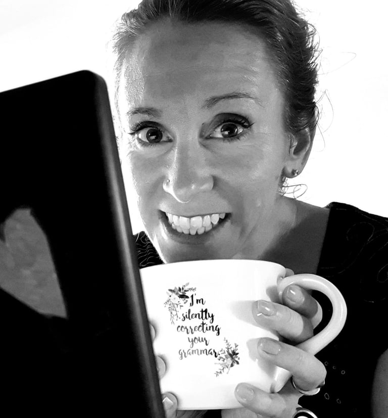 Author-editor K.A. Hough smiles as she holds a mug which reads, I'm silently correcting your grammar