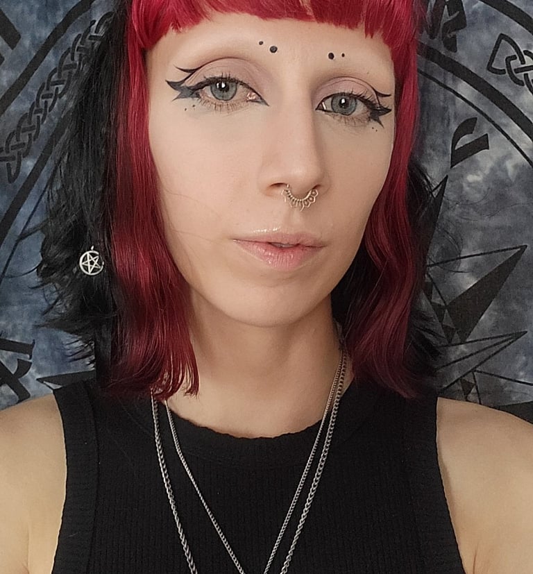 A woman with vibrant red and black hair, gothic winged eyeliner, and pentagram jewelry.
