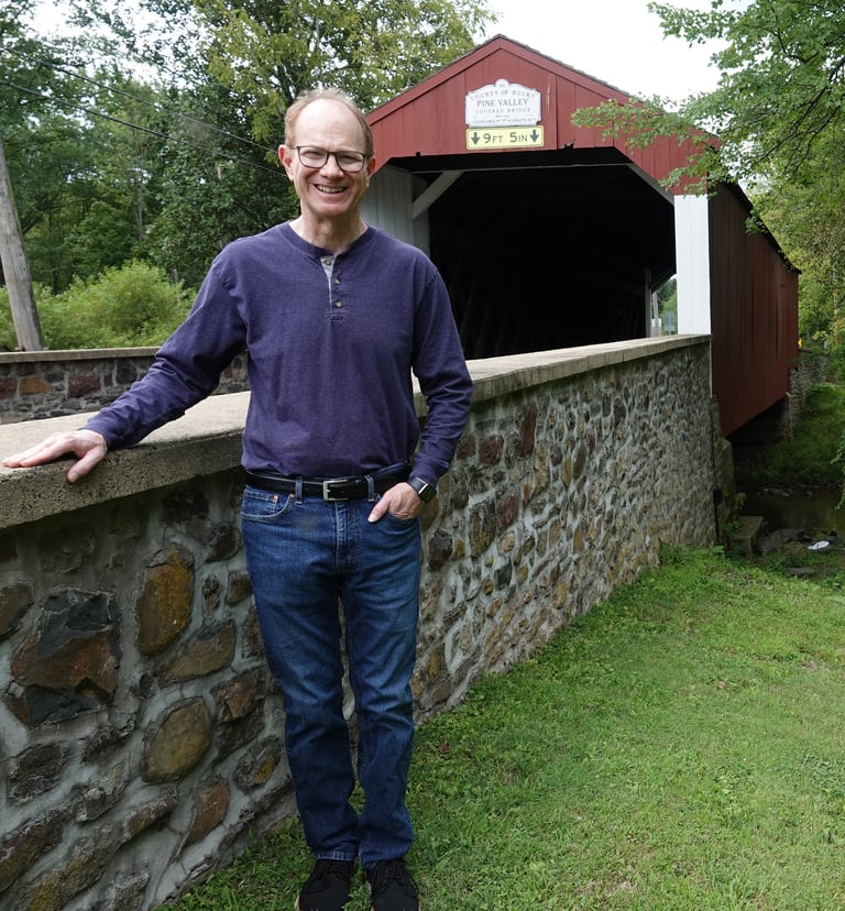 Picture of Michael leaning on a stone wall of a covered bridge in Pennsylvania
