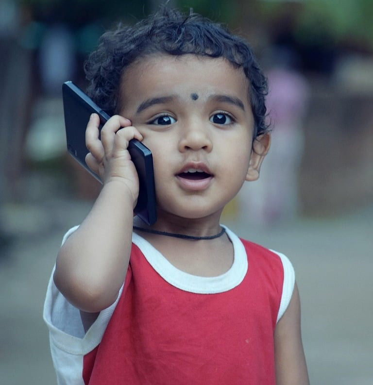 Young Indian toddler with curly hair holding a smartphone to his ear making a phone call.