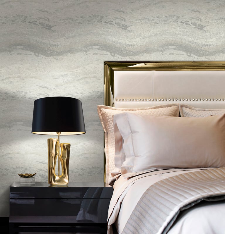 Luxury bedroom with grey marble wallpaper, gold headboard, and black designer bedside lamp.