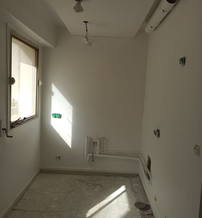 Pièce vide en rénovation avec murs blancs, tuyaux de plomberie apparents et câblage électrique
