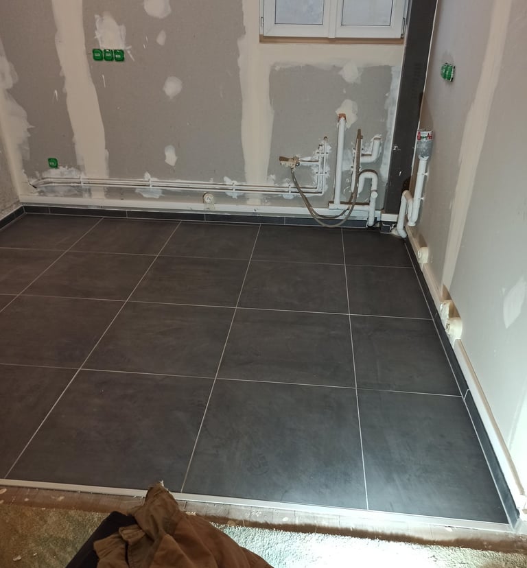 Installation de carrelage gris foncé dans une pièce en rénovation avec plomberie et prises électriqu