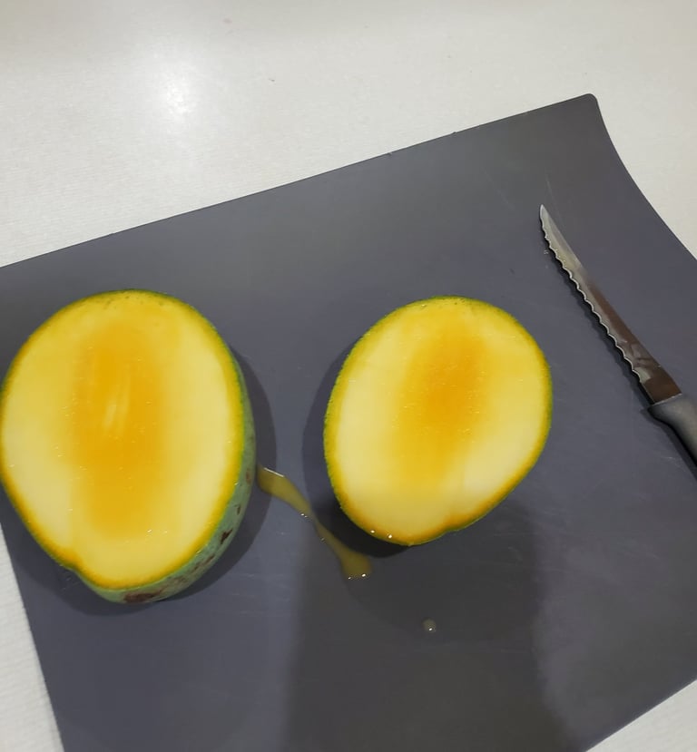 Two fresh 'Sugarloaf' mango halves showing yellow pulp on a black grown at Luro Grove, in Miami-Dade