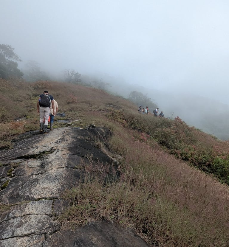 A group of hikers with backpacks trekking along a rocky mountain ridge through thick white mist and fog.