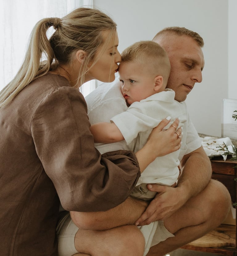 three people, one adult holding a child while another kisses the childs forehead