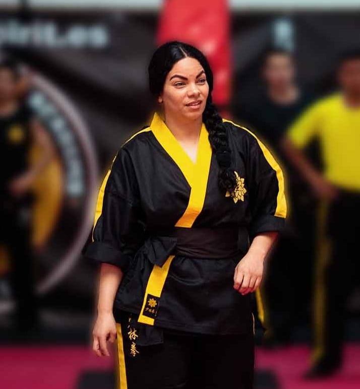 a woman in a black and yellow uniform is standing in a karate pose