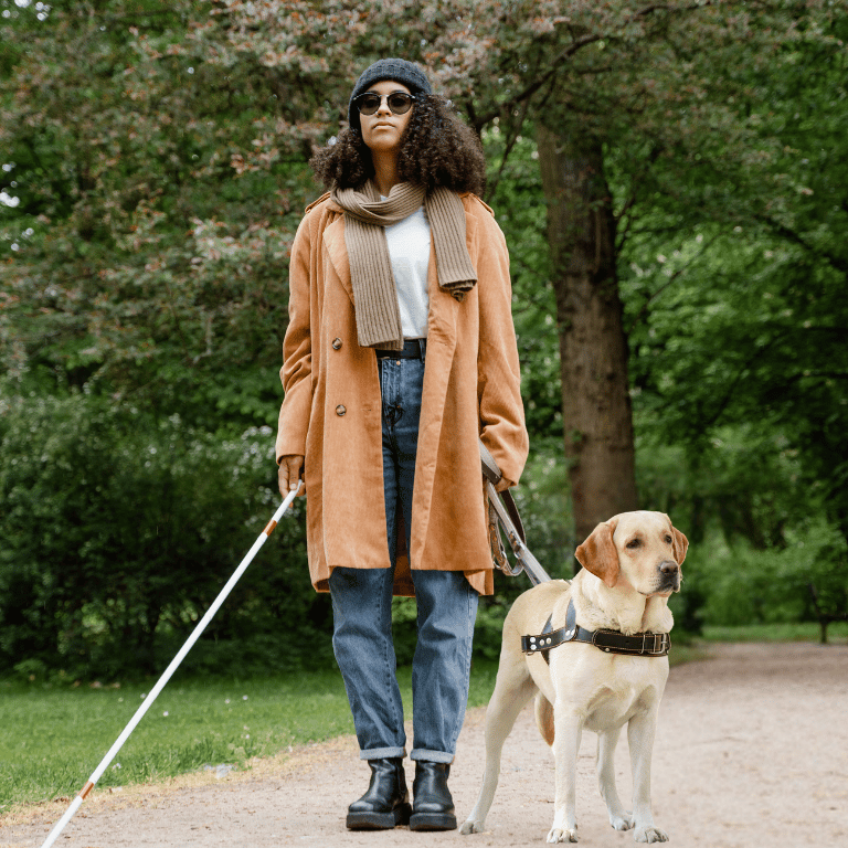 Legally blind disabled woman walking in a park with her guide dog and cane, both non optical aids