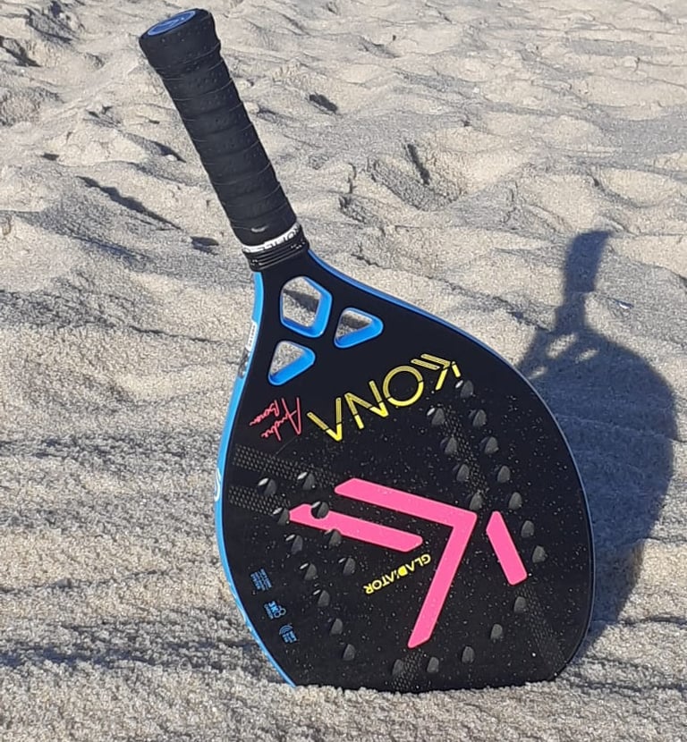 Raquete de beach tennis descansando sobre a areia, com parte da sua cabeça enterrada na praia.