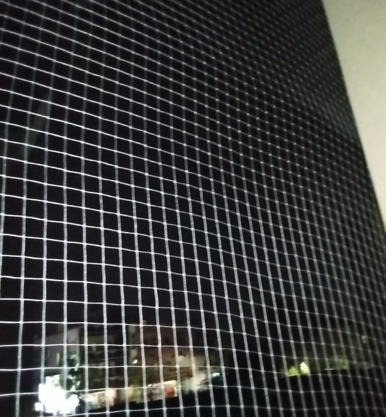 Technician carefully fitting a pigeon net frame on a high-rise balcony.