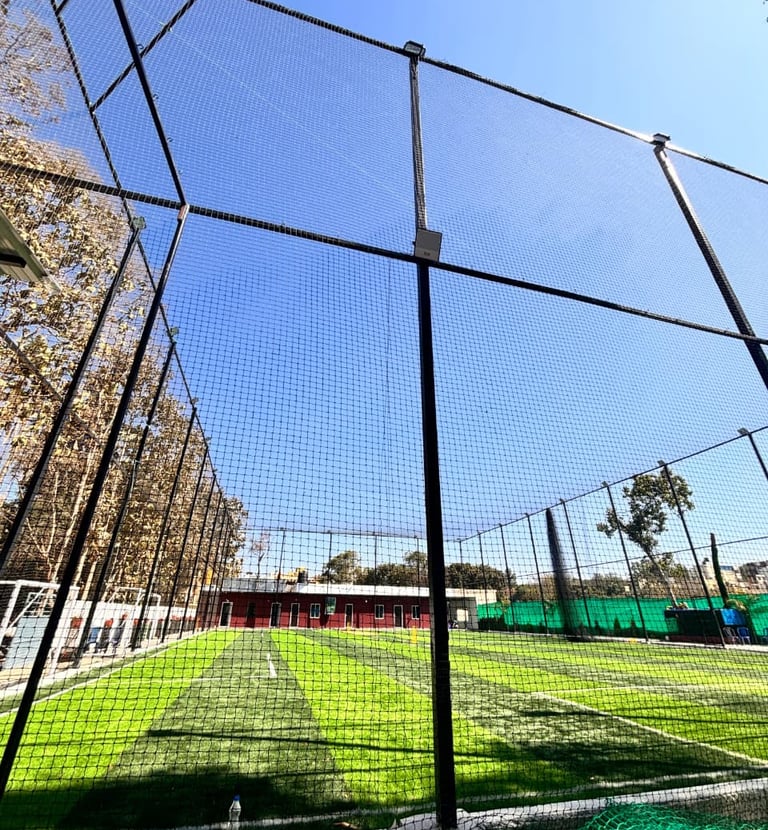 Technician securing a sports net tightly on metal poles under bright Chennai sunlight.