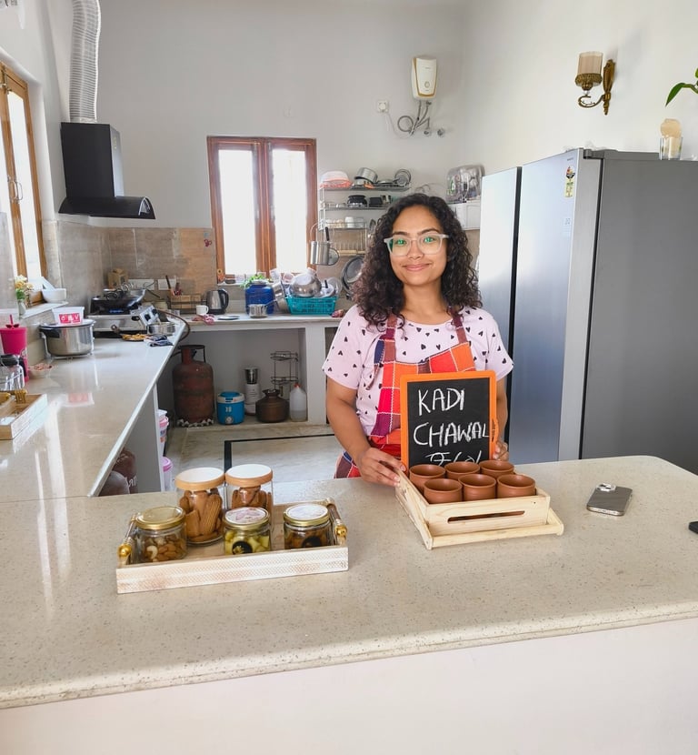 A smiling chef in a modern kitchen presenting Kadhi Chawal in traditional clay pots on a wooden tray.