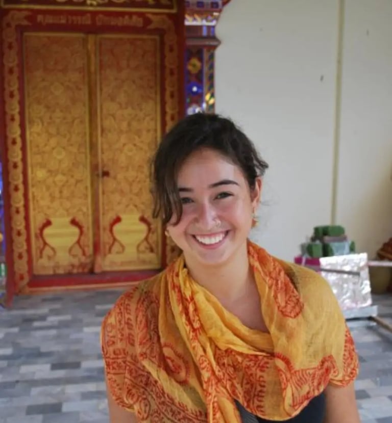 Clara Coelho em frente a templo na Índia, anos após sua primeira formação. Sorriso genuíno e vivênci