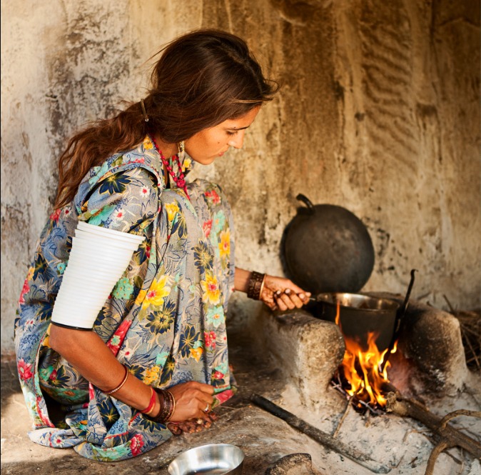 a woman in a floral print dress is cooking in a pot