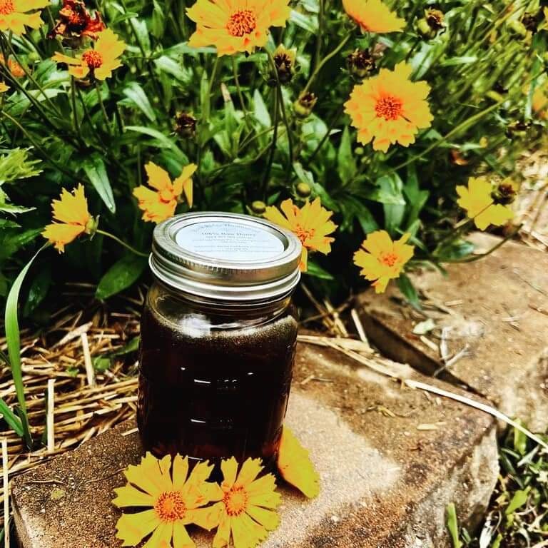 jar of honey on block sitting in yellow flowers