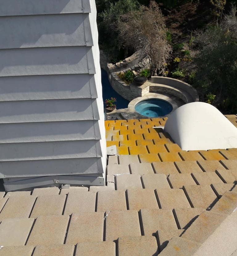 Aerial view of a gray shingle roof and chimney overlooking a luxury swimming pool and hot tub.