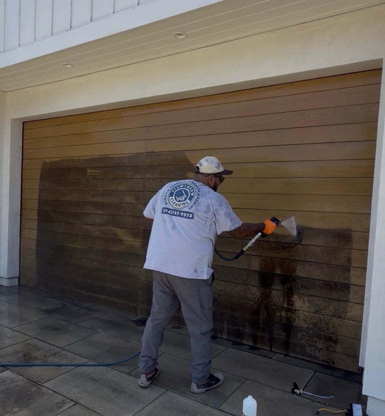 A professional technician power washing a wooden garage door to remove dirt and stains.