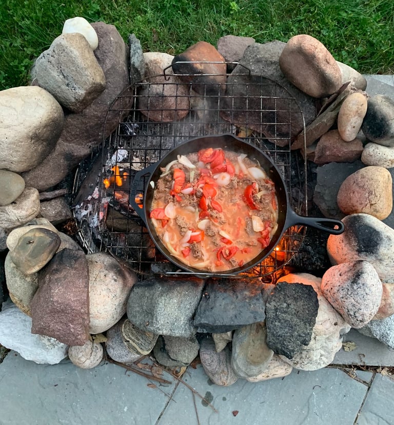 Homemade chili in a cast iron skillet cooking over a campfire surrounded by a stone fire ring